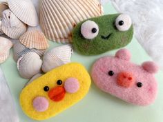 three small felt animals sitting next to seashells