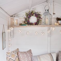 a bench with pillows and candles on it in front of a white wall, decorated with wreaths