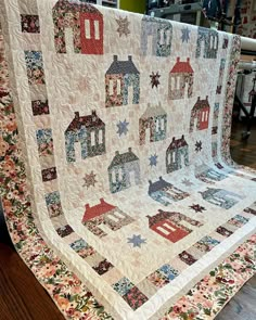 a quilted blanket with houses on it sitting on top of a wooden floor next to a chair