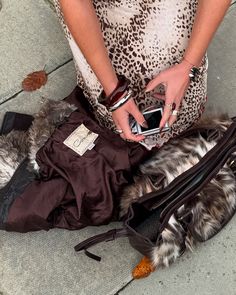 a woman holding a cell phone next to a purse on the ground with other items around her