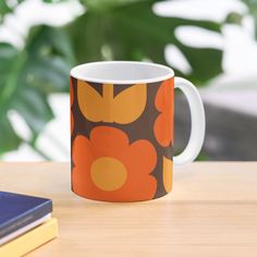 an orange and brown flowered coffee mug sitting on top of a wooden table next to a book