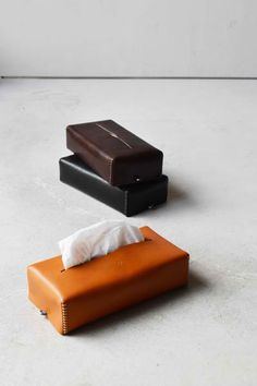 two pieces of leather sitting on top of a white floor next to each other, one with a tissue dispenser in it