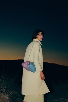 a woman is standing in the sand with a handbag on her shoulder and looking off into the distance