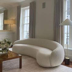 a living room filled with furniture next to two large windows and a lamp on top of a table