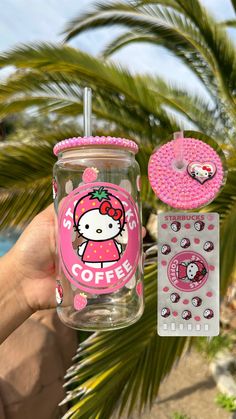 a person holding up a hello kitty coffee cup next to a sticker and palm tree