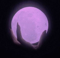 someone is holding the moon in their hands with purple light on it's face