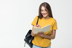 a girl in a yellow shirt is holding a black bag and writing on a book