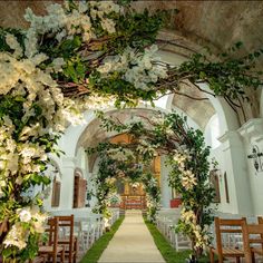 an outdoor wedding ceremony with white flowers and greenery on the arch over the aisle