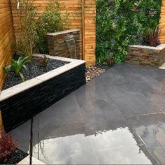 an outdoor garden with wooden walls and plants on the sides, surrounded by black slate slabs