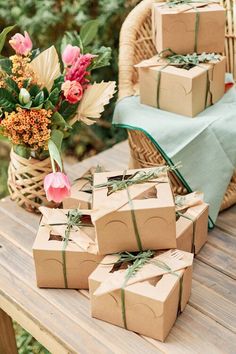 several boxes wrapped in brown paper tied with green ribbon on a wooden table next to flowers