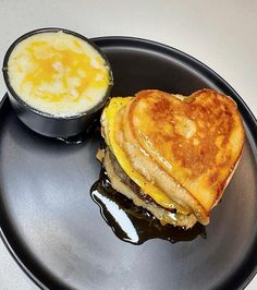 a heart shaped sandwich on a black plate next to a bowl of sauce and an egg