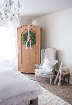 a bedroom with a chair, armoire and wreath on the door