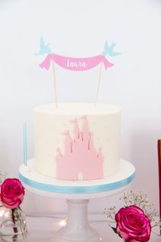 a white cake with pink frosting and a name on top sitting on a table