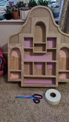 a dollhouse made out of cardboard with scissors and tape on the floor next to it