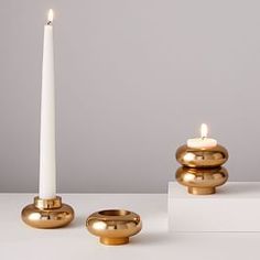 two gold candles sitting next to each other on top of a white table with one candle in the middle