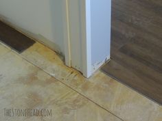 a white refrigerator sitting on top of a wooden floor next to a wall and door