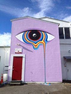 an eye painted on the side of a building with blue sky and clouds in the background