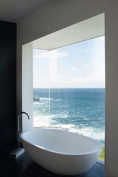 a bath tub sitting in front of a window next to the ocean on top of a tiled floor