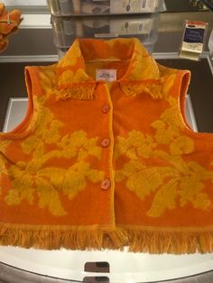 an orange vest with yellow flowers and fringes on display in a glass case at a store