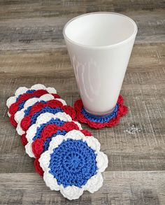 red, white and blue crocheted coasters next to a cup on a wooden table