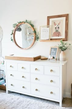 a white dresser sitting in a living room next to a wall with pictures on it