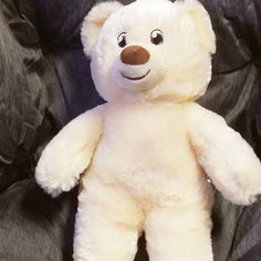 a white teddy bear sitting on top of a black chair with its eyes wide open