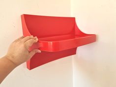 a hand is holding a red shelf on the wall