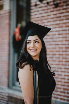 a woman wearing a graduation cap and gown standing in front of a brick building smiling at the camera