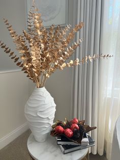 a white vase filled with red and gold ornaments on top of a table next to a window