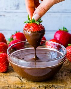 someone dipping a strawberry into chocolate in a bowl