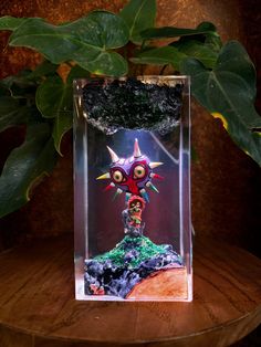 a glass box with a small figure inside it on a table next to a plant