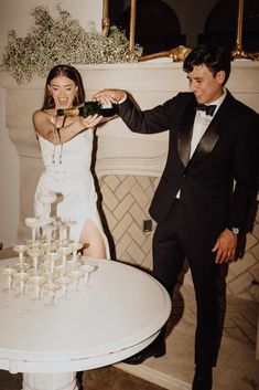 a man and woman standing next to each other in front of a table with glasses on it