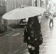 a woman in kimono walking down the street with an umbrella on top of her head