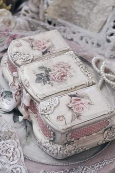 three decorative boxes sitting on top of a lace covered tablecloth with flowers and leaves