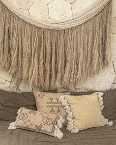 a bed topped with pillows next to a stone wall covered in tassels and fringe