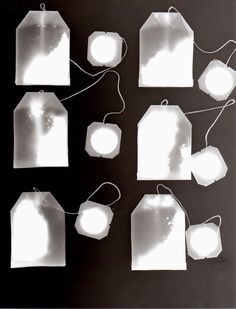 six white tags hanging from strings with light shining through them on a black background,