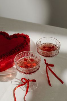 two wine glasses with red hearts on them next to a heart shaped cake