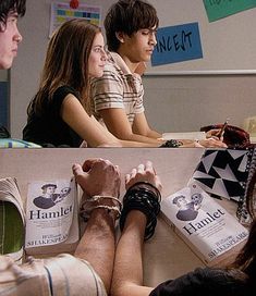 three people sitting at a table with books and papers in front of them on their feet