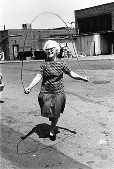 an older woman jumping with a skipping rope in front of a pink sign that says, you can't help getting older, but you don't have to get old