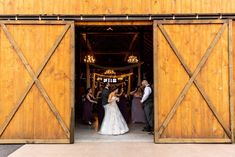 a bride and groom standing in front of a barn door with their wedding party around them