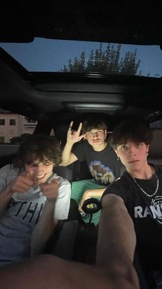 three boys sitting in the back of a car with their hands up and one boy pointing at something