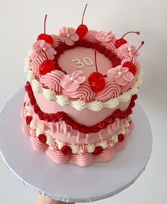 a heart shaped birthday cake with cherries on the top is being held by a person