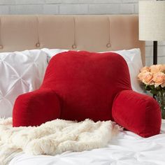 a large red chair sitting on top of a bed next to pillows and flowers in vases