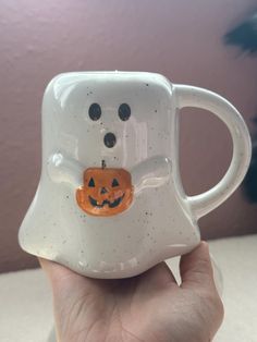 a hand holding a white coffee mug with a pumpkin on it