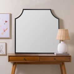 a mirror sitting on top of a wooden table next to a lamp and pictures hanging on the wall