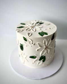 a white cake with green leaves and flowers on it