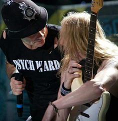 a man holding a guitar while standing next to a woman with long blonde hair and wearing a black hat