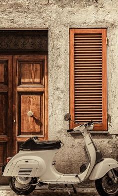 a white scooter parked in front of a building with shutters on the windows