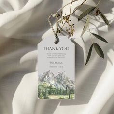 a thank card with an image of the mountains and trees on it is hanging from a twig