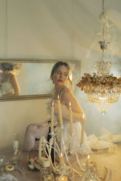 a woman sitting at a table in front of a chandelier with candles on it